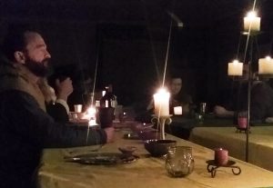photo of bearded man in profile at a table with medieval feast gear and candles 